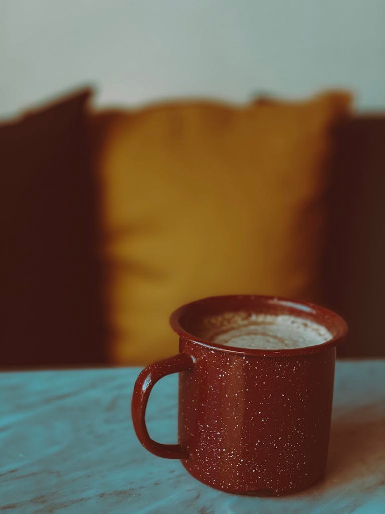 A warm, inviting red mug filled with creamy coffee on a rustic table.